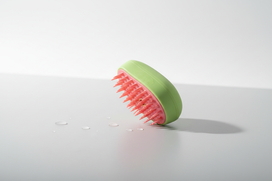 Green silicone pet spray massage brush with pink bristles on light grey surface with water droplets